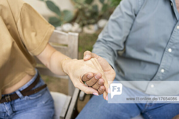 Couple sitting on chair holding hands at back yard