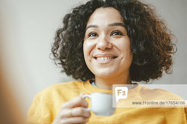 Smiling beautiful woman with curly hair holding coffee cup