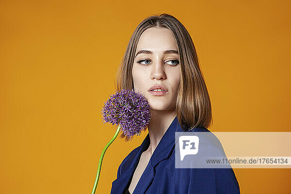 Beautiful young woman with allium flower against orange background