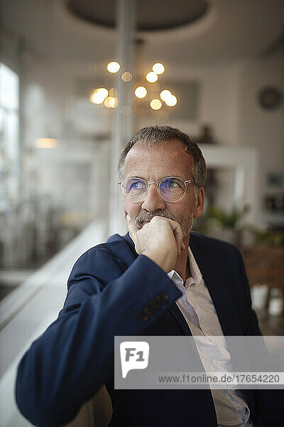 Thoughtful businessman wearing eyeglasses sitting in cafe