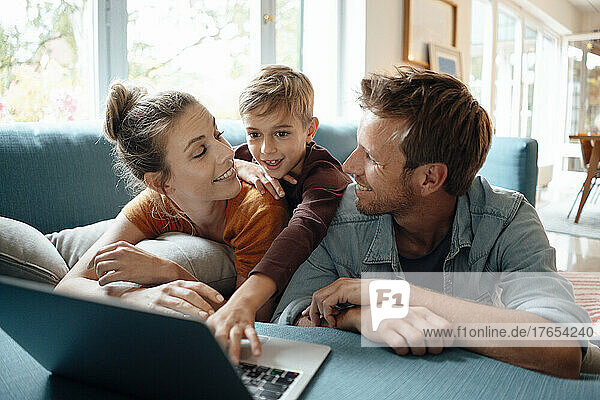 Lächelnder Vater und Mutter schauen den Sohn an  der zu Hause einen Laptop benutzt