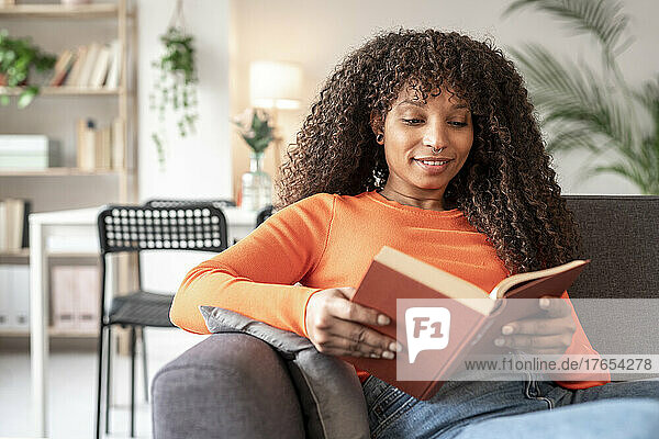 Young woman reading book sitting on sofa in living room