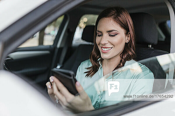 Glückliche Geschäftsfrau benutzt Smartphone im Auto