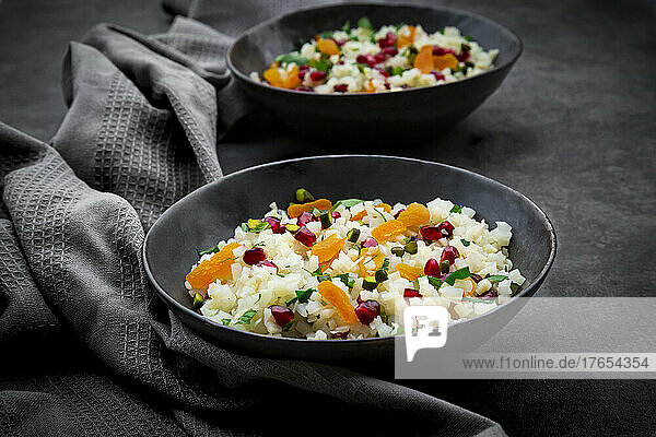 Studio shot of two bowls of cauliflower salad with apricot  pomegranate seeds  pistachios  mint and parsley