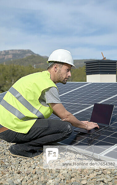 Engineer with laptop by solar panels on sunny day