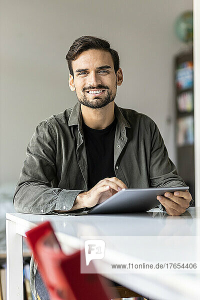Lächelnder Mann mit Tablet-PC sitzt zu Hause am Tisch