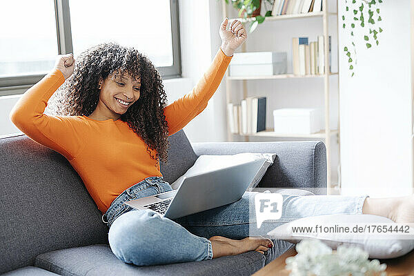Lächelnde gestikulierende Frau  die zu Hause mit Laptop auf dem Sofa sitzt