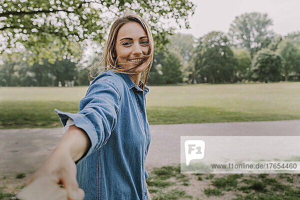 Smiling young woman pulling friend's hand in park