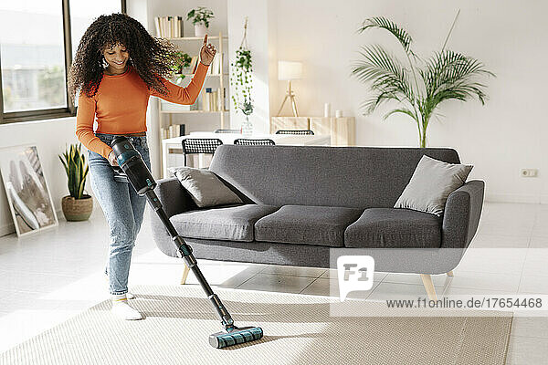 Smiling young woman with vacuum cleaner dancing in living room at home
