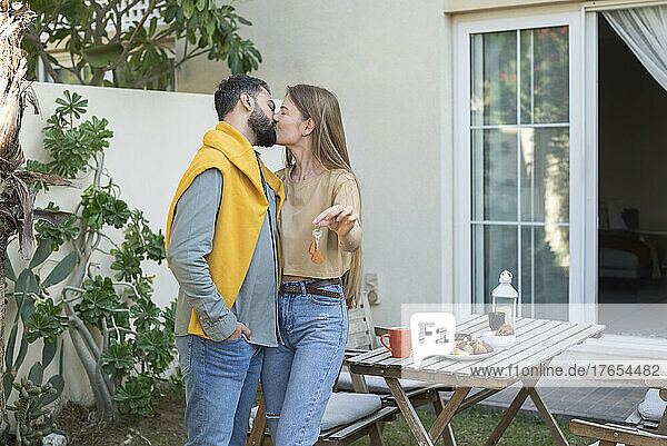 Man kissing woman on mouth holding key by house in back yard