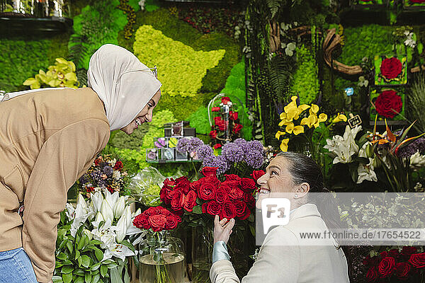 Happy woman showing roses to colleague at flower shop