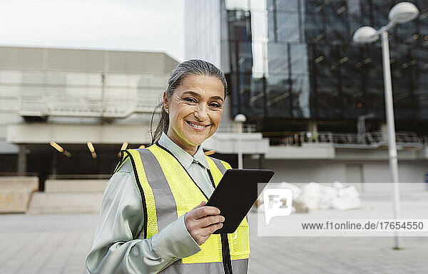 Happy engineer with tablet PC standing outside modern building