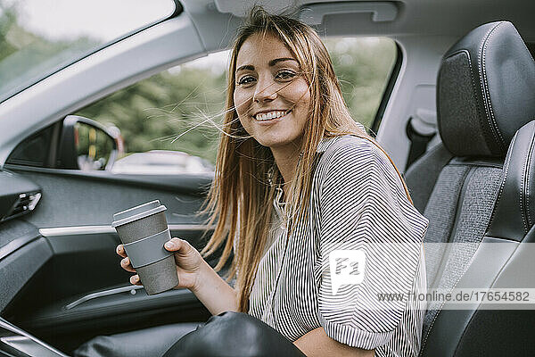 Lächelnde Frau mit Einwegkaffeetasse sitzt im Auto