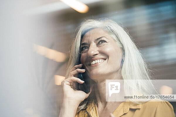 Glückliche Geschäftsfrau mit grauen Haaren  die im Büro mit dem Mobiltelefon spricht