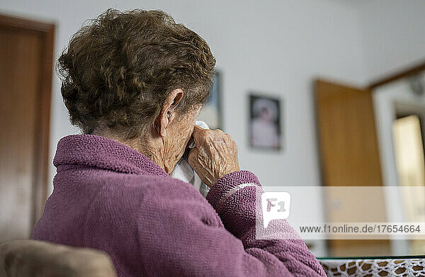 Senior woman rubbing eyes with tissue at home