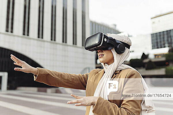 Young businesswoman wearing virtual reality simulator gesturing at office park