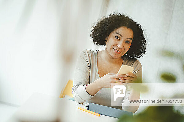 Lächelnder Freiberufler mit Smartphone am Tisch sitzend