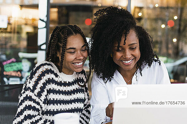 Happy colleagues sharing laptop sitting at cafe