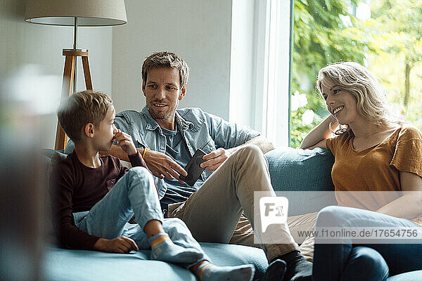 Son talking with mother and father sitting on sofa in living room