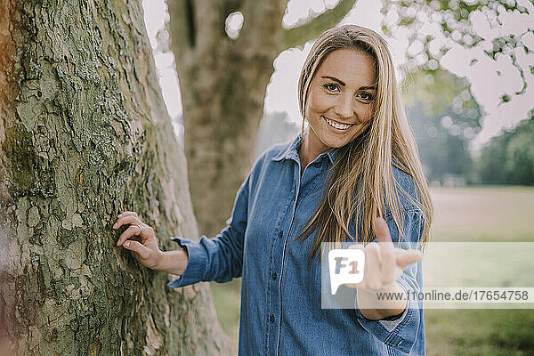 Smiling woman gesturing by tree in park