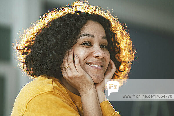 Happy beautiful woman with curly hair sitting with head in hands at home