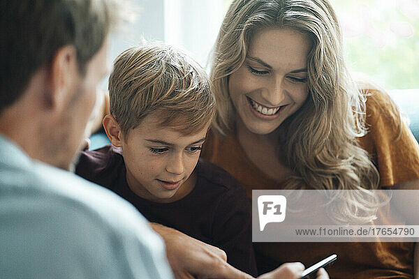 Man sharing smart phone with son and woman at home