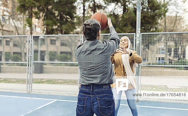 Businesswoman playing basketball with young colleague at sports court