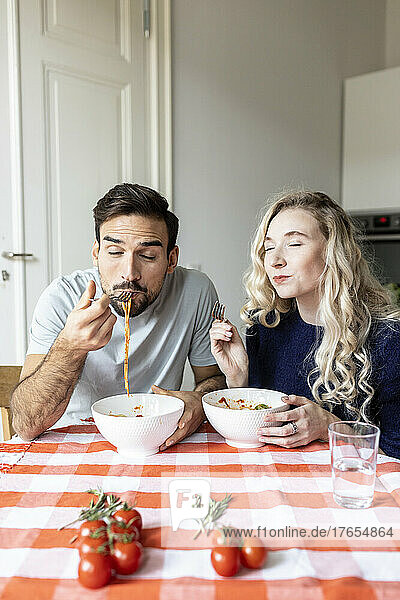 Hungry couple eating noodles on dining table at home