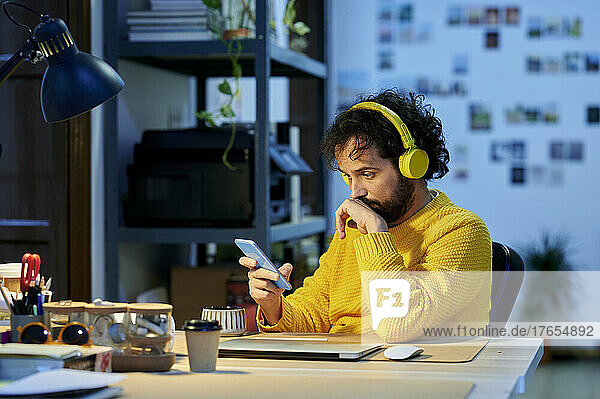 Businessman listening music through wireless headphones using smart phone in office