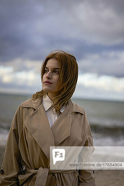 Beautiful young woman wearing coat standing at beach