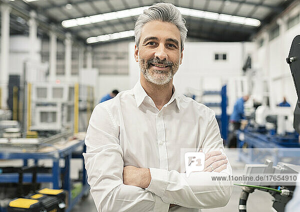 Smiling businessman standing with arms crossed in factory