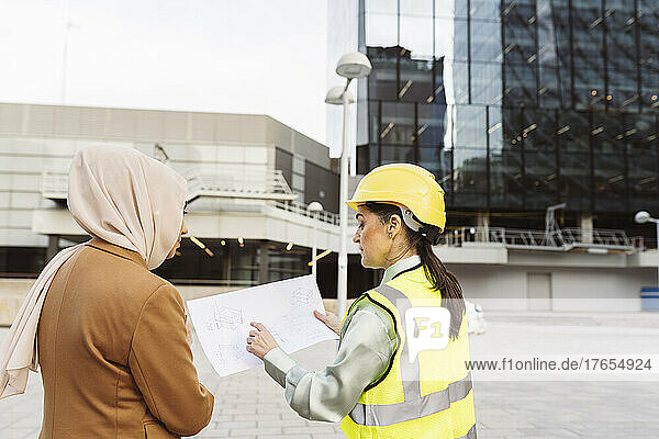 Architect discussing over blueprint with businesswoman outside modern building