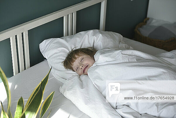 Smiling boy with blanket sleeping in bed at home