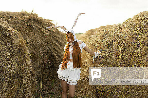 Young woman wearing rabbit costume ears standing amidst hay bales