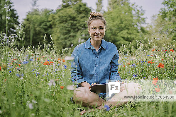 Smiling young woman with tablet PC sitting in meadow