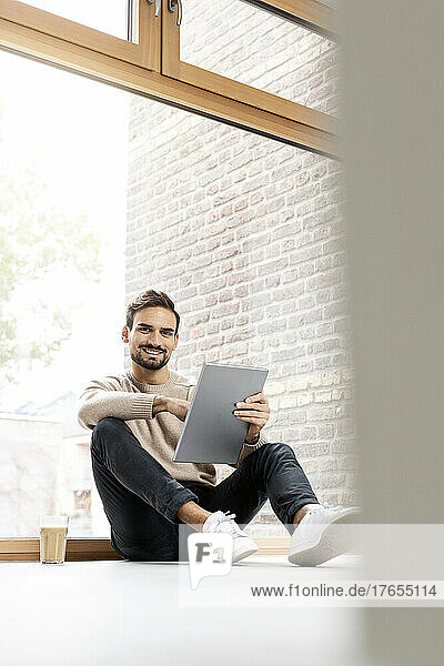 Man with tablet PC sitting in front of glass window