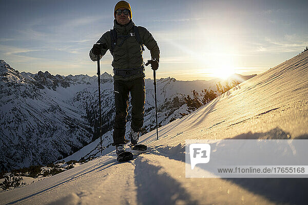Mann mit Skistock läuft bei Sonnenaufgang auf schneebedecktem Berg