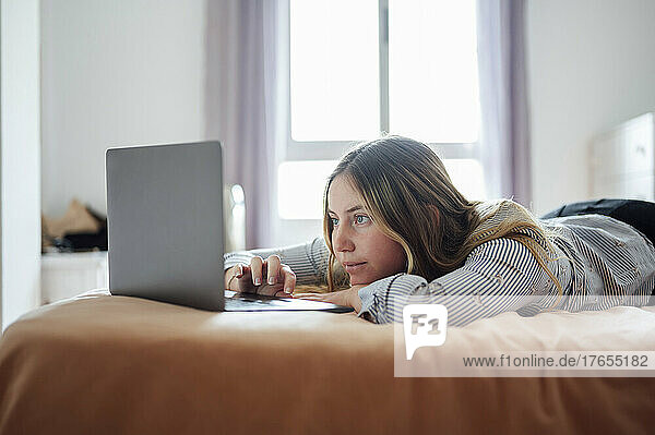 Junge Frau benutzt Laptop und liegt zu Hause im Bett