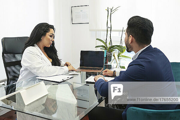 Dermatologist discussing over laptop with patient at desk in aesthetic clinic