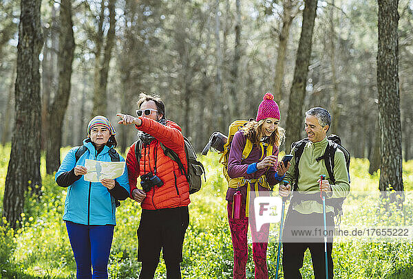 Man and woman with map standing by friends sharing smart phone in forest