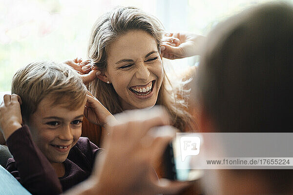 Cheerful woman with son photographed by man at home