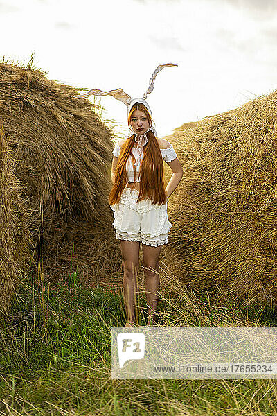 Young woman wearing rabbit costume standing amidst hay bales