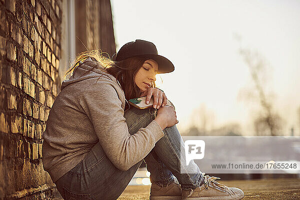 Waiting young woman with baseball cap sitting on the ground hugging knees