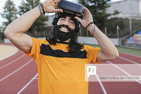 Happy man with virtual reality simulator standing on running track