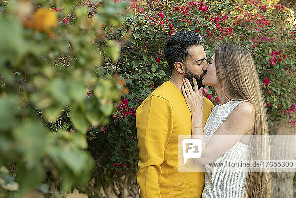 Couple kissing by plants in back yard