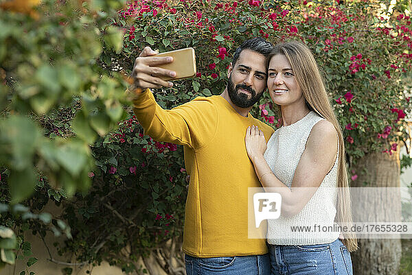 Man taking selfie with woman through smart phone in back yard