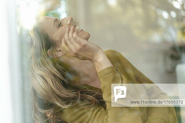 Blond woman with eyes closed laughing seen through glass