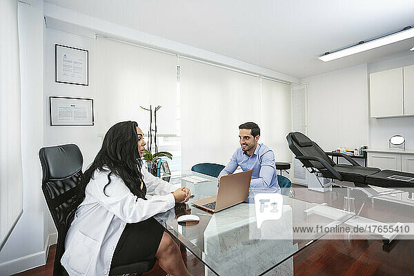 Dermatologist discussing with patient sitting at desk in aesthetic clinic