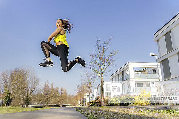 Woman wearing sports clothing jumping on footpath