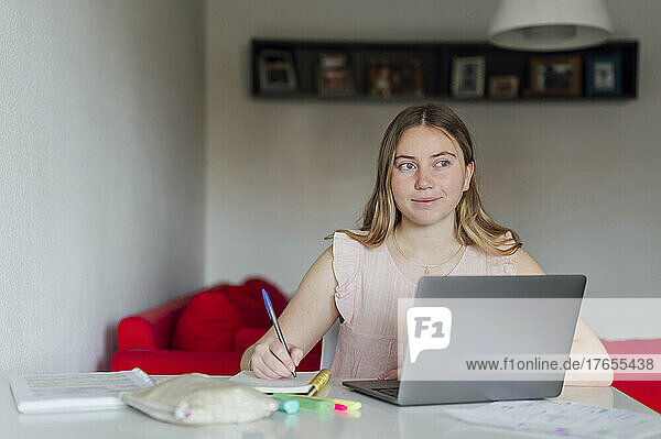 Smiling woman with note pad and laptop sitting at home